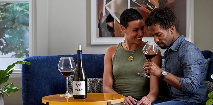 A couple enjoying WALT Pinot Noir together in a cozy setting at the WALT Napa tasting room in the Napa Oxbow. 